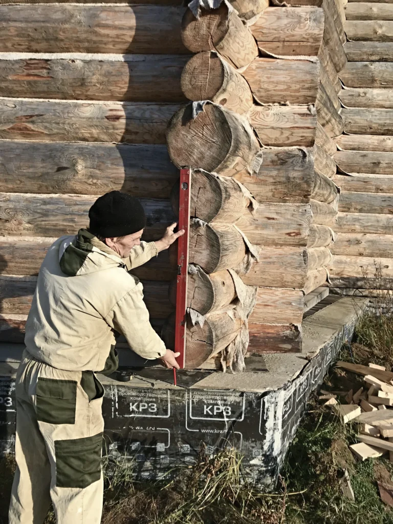Рабочий проверяет вертикальность угла сруба уровнем — Калужское шоссе